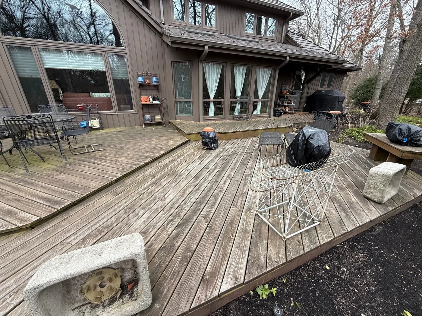 Large multi-level wood deck weathered to a dull silver-gray, with patio furniture pushed off to one side.