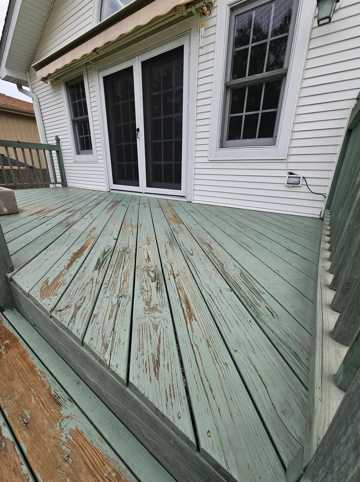 Deck with pale green paint peeling and flaking away, exposing bare wood along the boards.