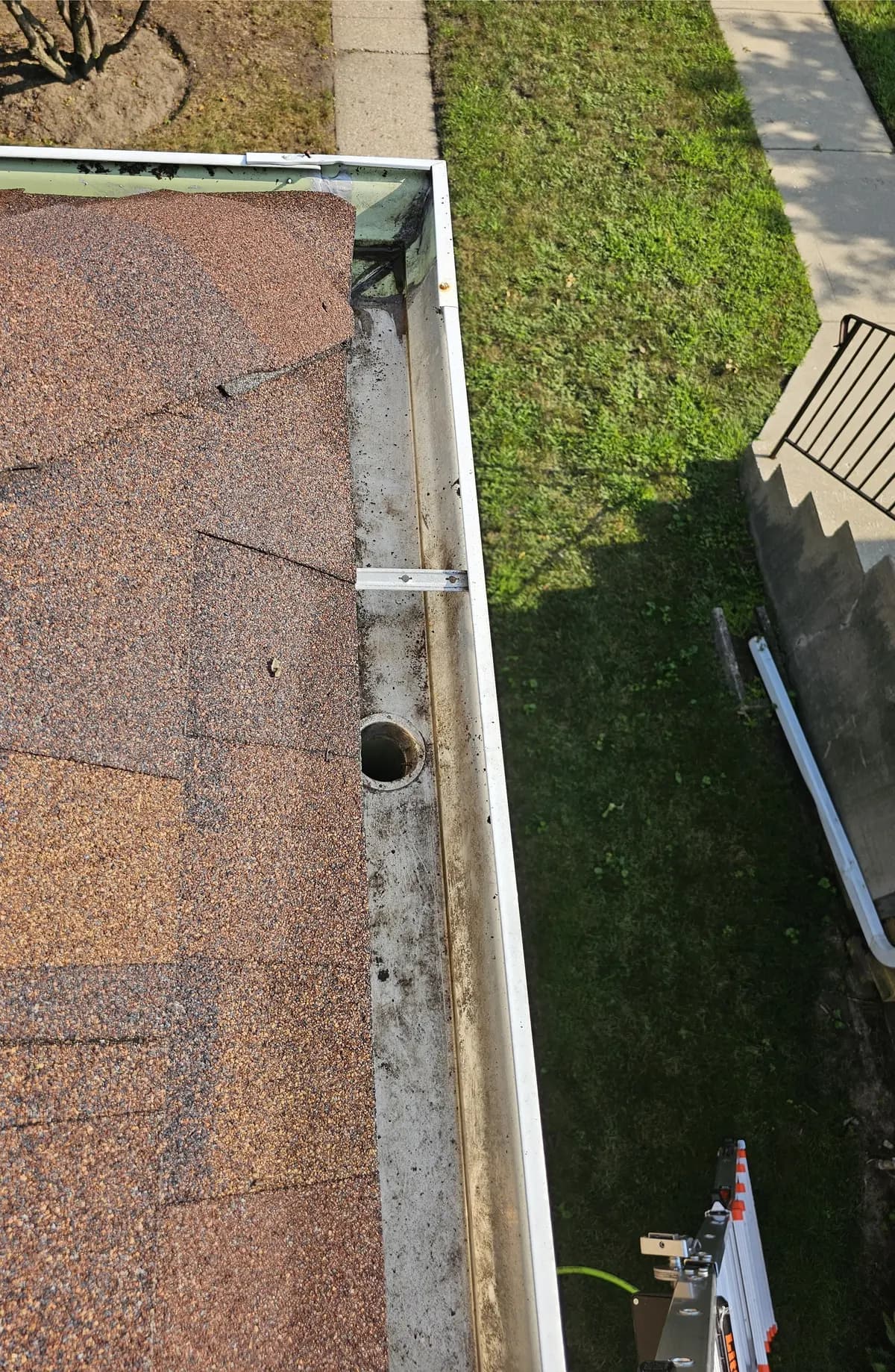 The same white gutter cleared to bare metal, with the downspout drop outlet fully open.
