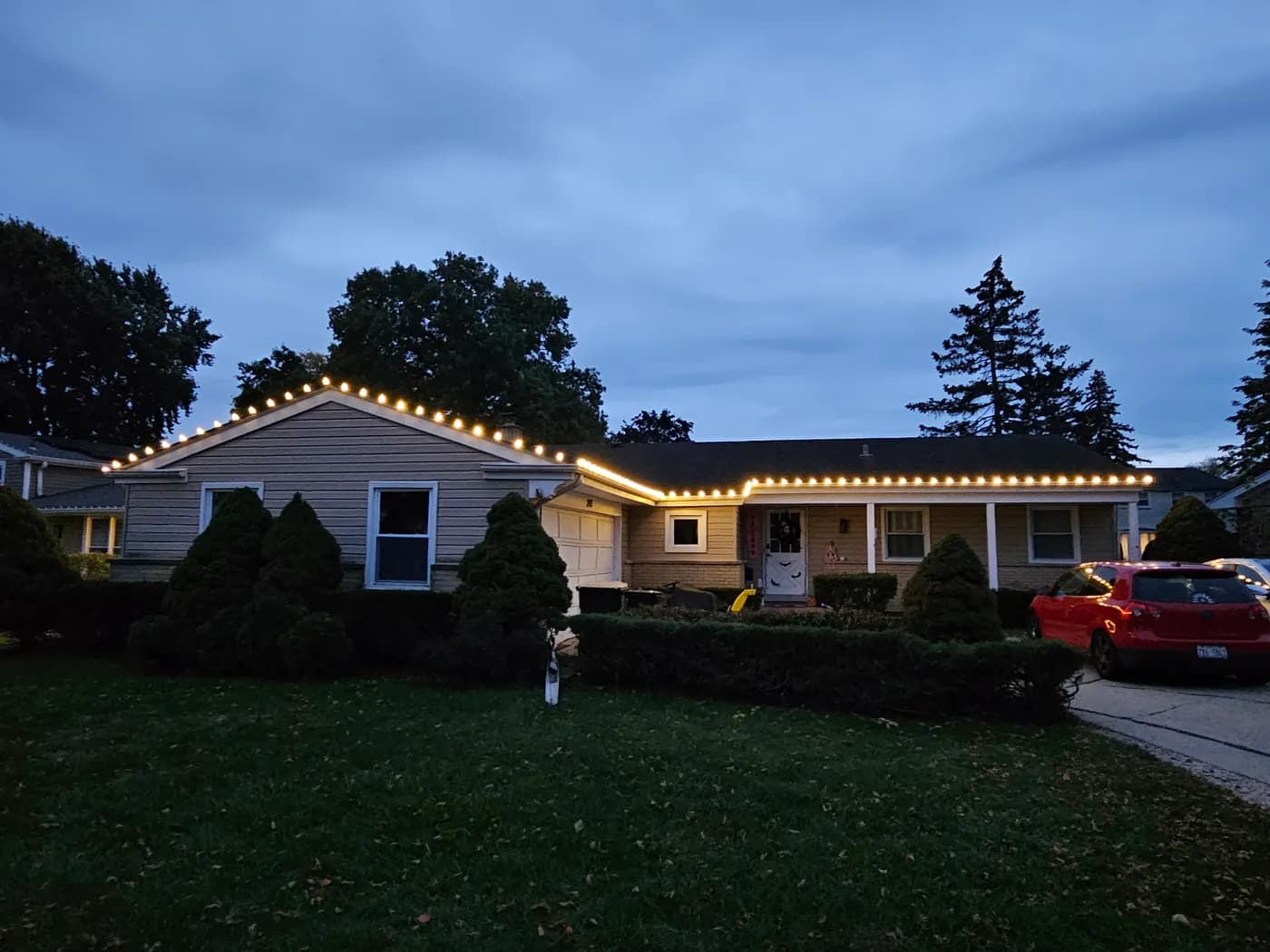 Single-story home at dusk with warm white bulbs running along the front gable and the full length of the roofline.