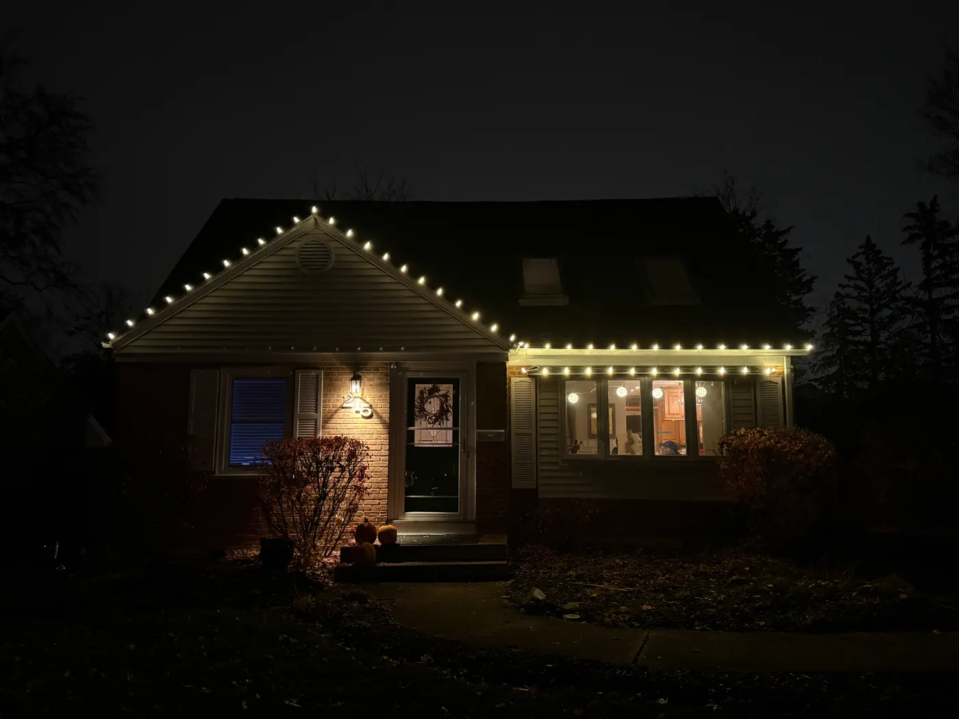 Brick and siding home after dark with warm white bulbs outlining the front gable peak and the eave over the front window.