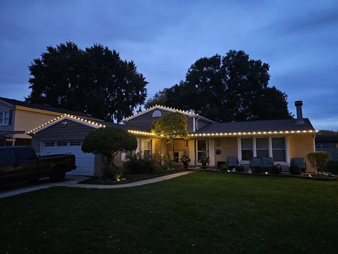 Yellow brick ranch house at dusk with warm white bulbs outlining the garage gable and the entire front roofline.