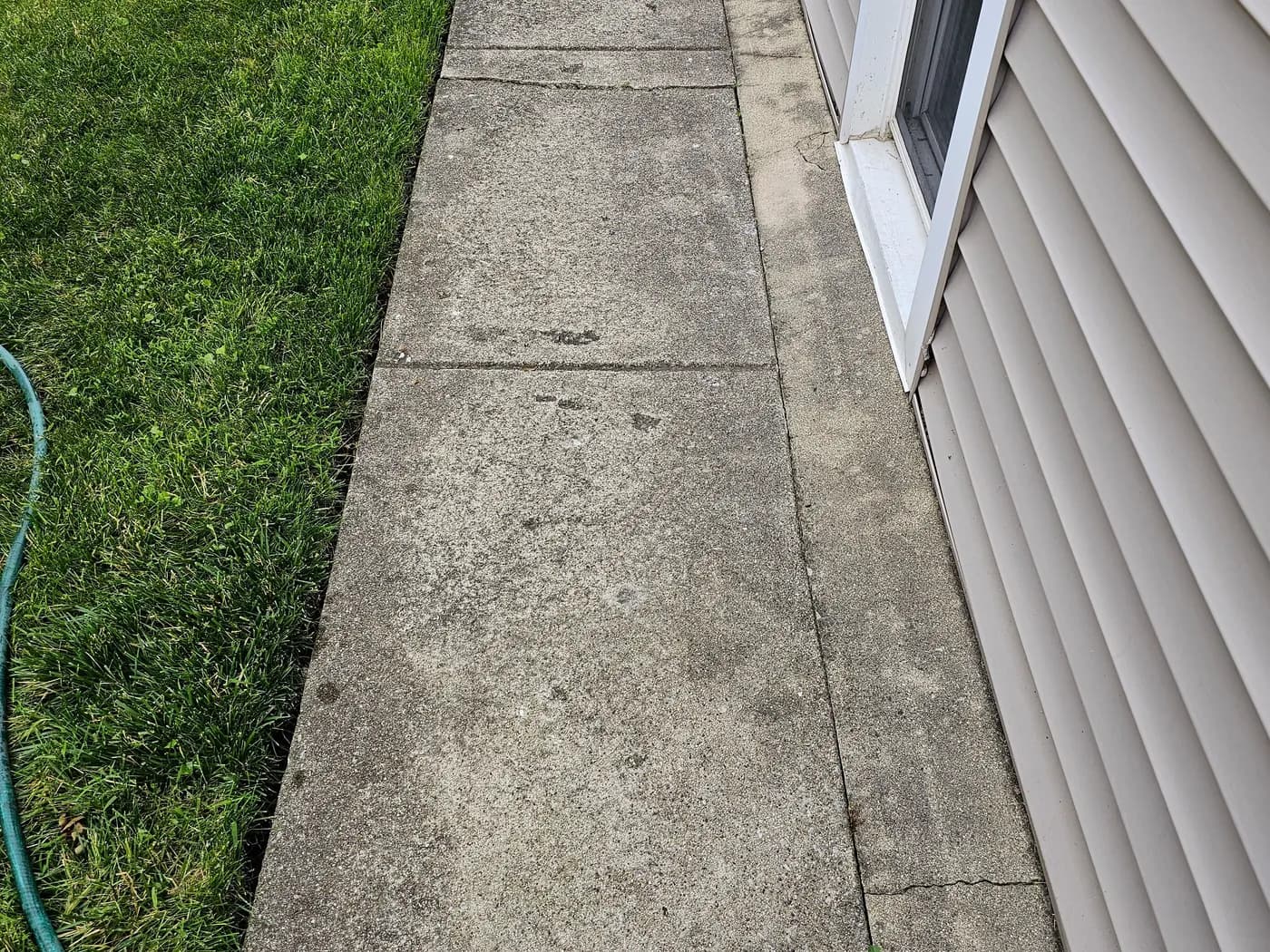 Concrete side walkway darkened by dirt and algae, with staining along the bottom of the siding.